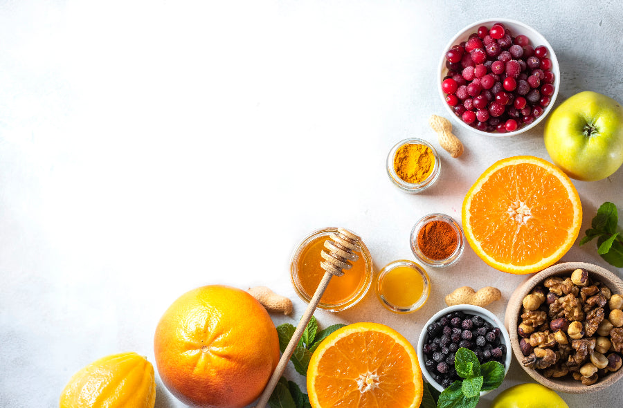 Bunte Auswahl an Superfoods – Orangen, Beeren, Nüsse, Honig, Kurkuma und Apfel auf hellem Untergrund