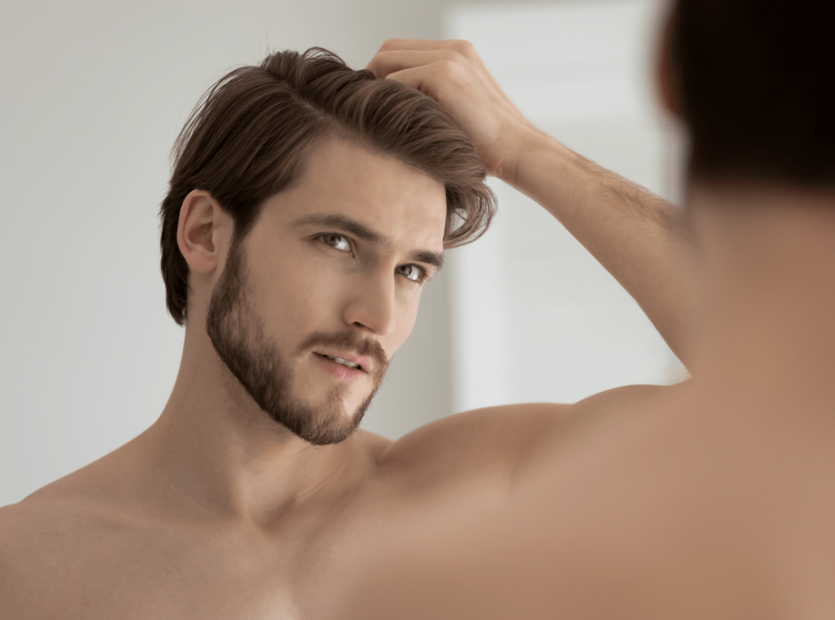 Junger Mann prüft Haaransatz vor dem Spiegel – Thema Haargesundheit und Haarbehandlung bei MYH&B