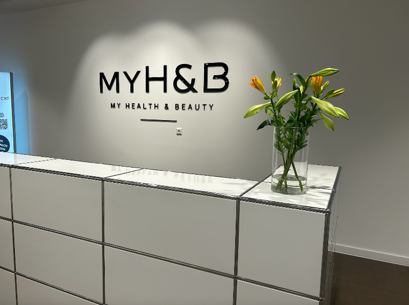 Empfangstresen von MYH&B mit einem frischen Blumenstrauß und Markenlogo an der Wand.