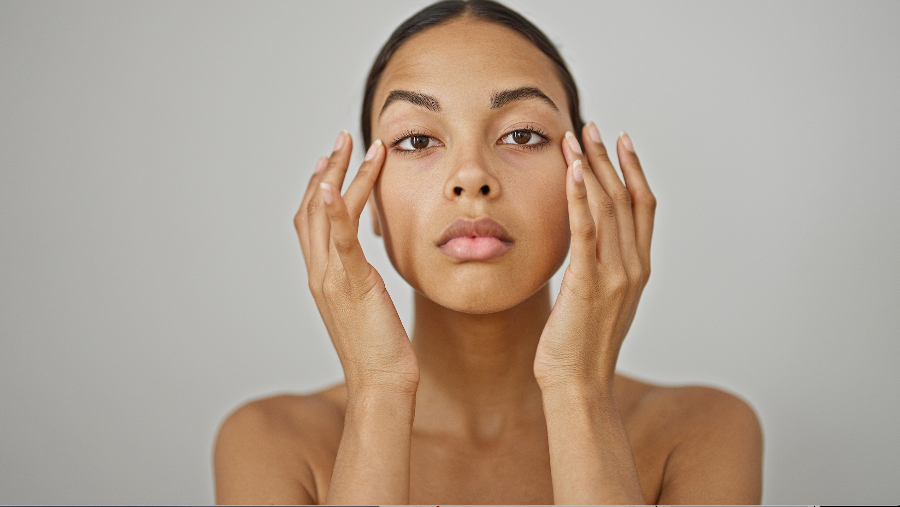 Junge Frau mit dunkler Haut betont ihre Augenpartie mit beiden Händen.