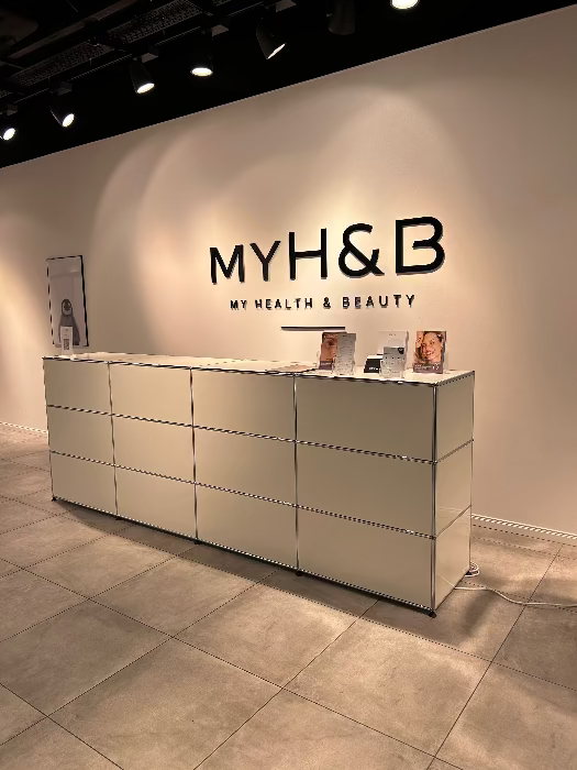 Minimalistischer Empfangsbereich bei MYH&B mit heller Theke und Markenlogo an der Wand