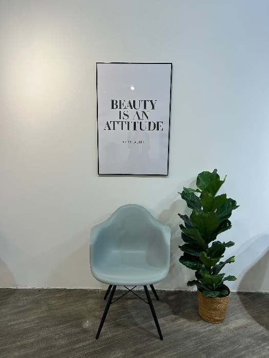 Wartebereich bei MYH&B mit Stuhl, Pflanze und Poster mit der Aufschrift "Beauty is an Attitude"