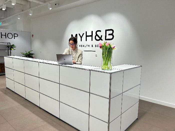 Empfangsbereich MYH&B mit moderner Theke, Blumenstrauß und Mitarbeiterin.