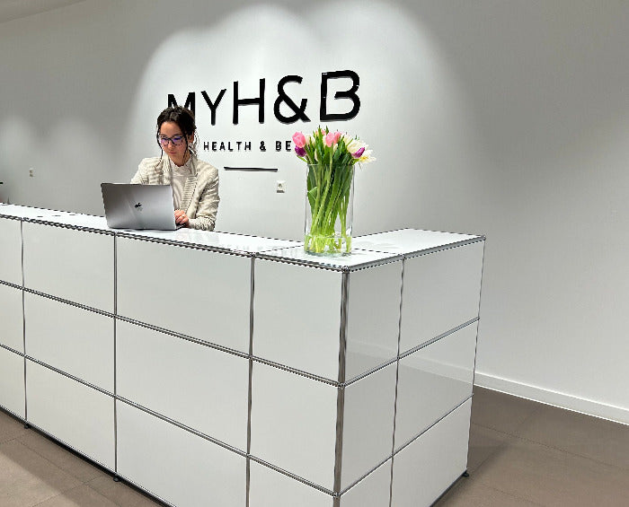 Empfangsbereich von MYH&B mit moderner Theke, Blumenstrauß und Mitarbeiterin am Laptop.
