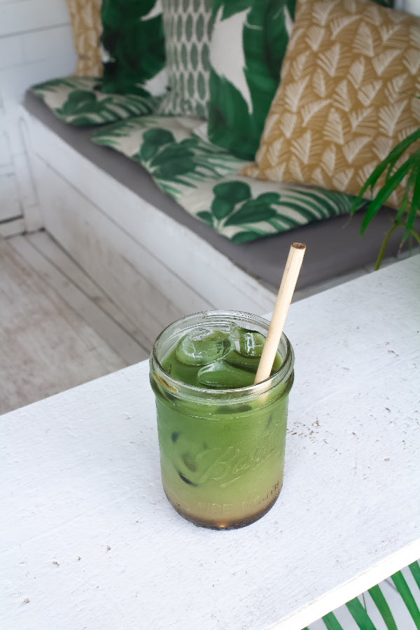 Erfrischender grüner Matcha-Drink mit Eis im Glas, serviert mit Bambusstrohhalm im tropischen Lounge-Ambiente