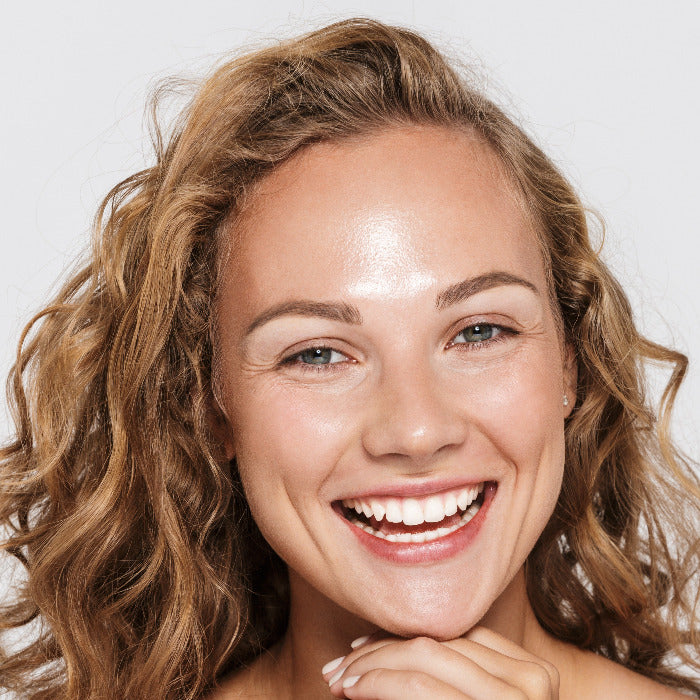 Strahlende Frau mit gesunder Haut und lockigem Haar – natürliches Lächeln und Glow