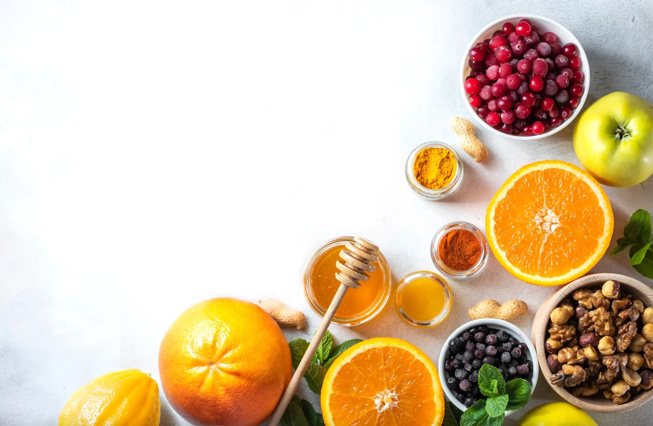 Gesunde Lebensmittel wie Orangen, Honig, Beeren und Nüsse auf heller Fläche