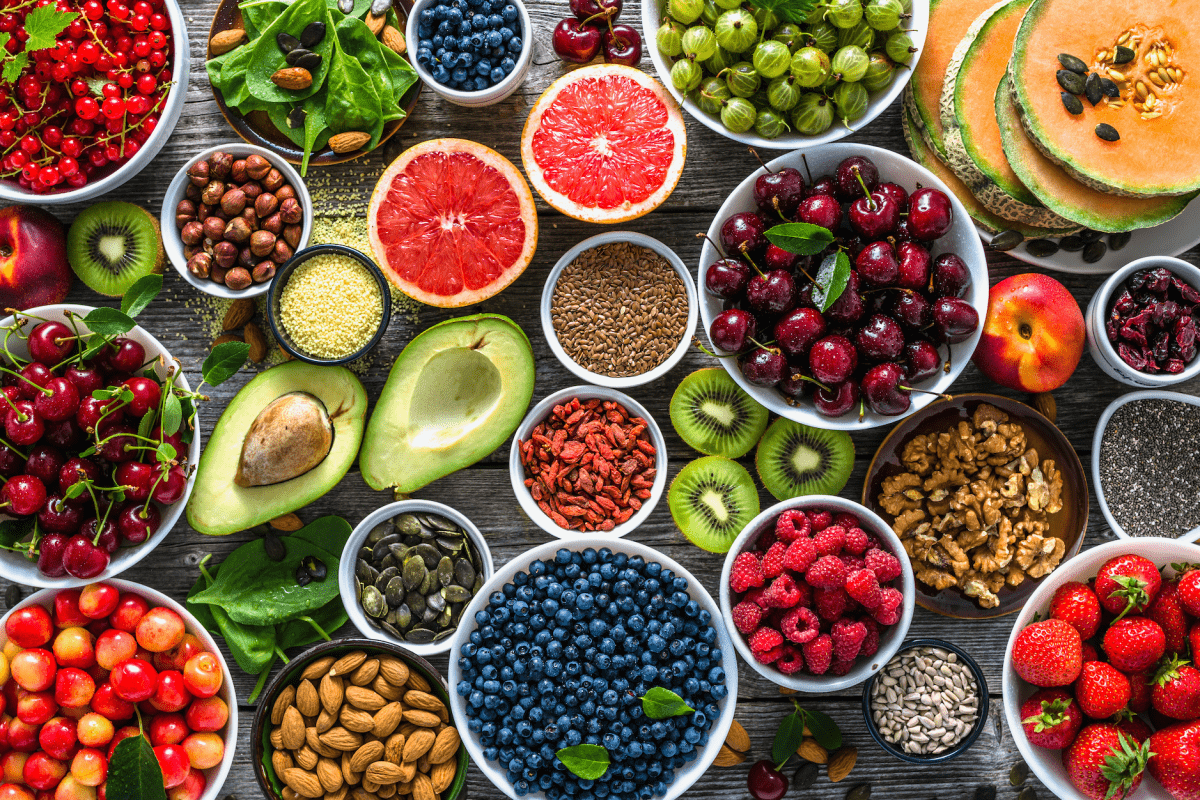 Bunte Auswahl an Superfoods und frischen Früchten – Beeren, Avocado, Nüsse, Samen und Blattgemüse auf Holztisch